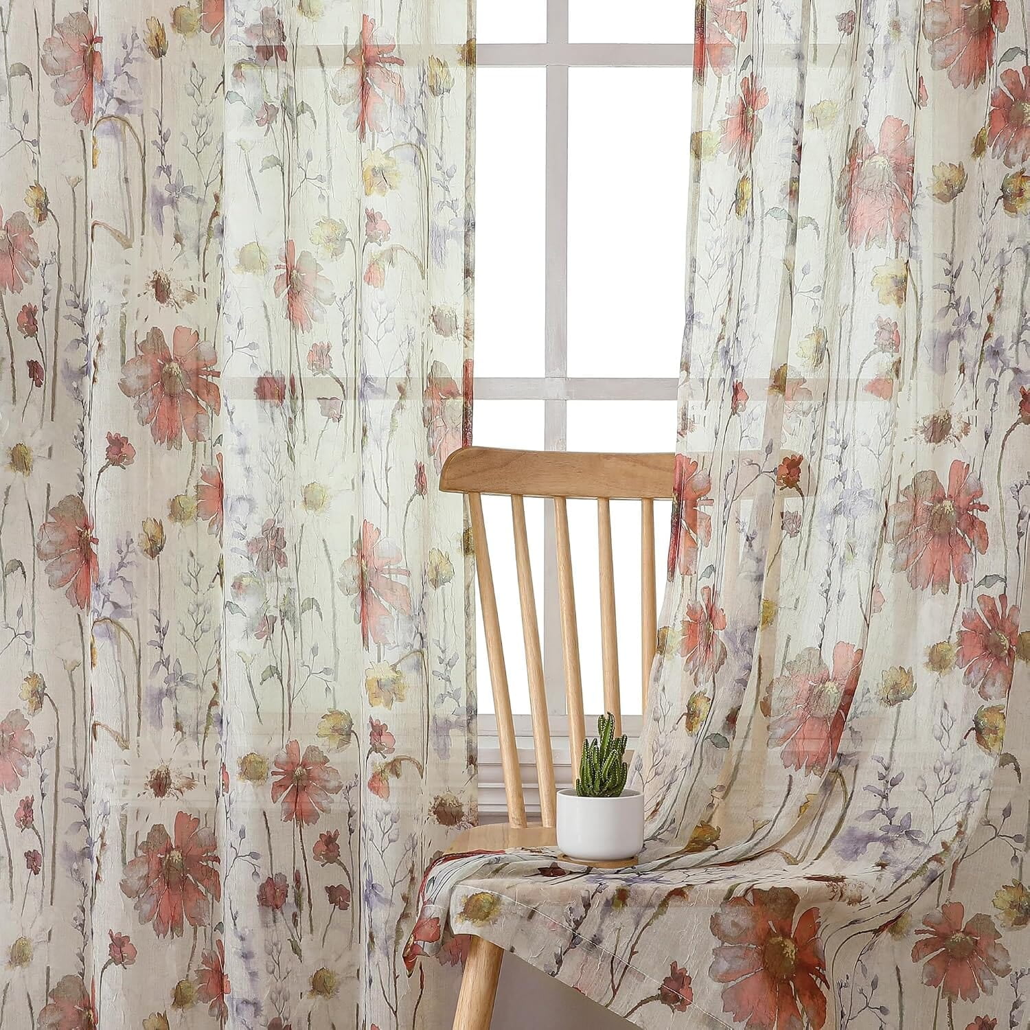 A close-up room view of crinkled translucent curtains with a multicolor floral print; full headers and hems are outside the image